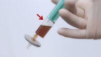 A brownish solution in a syringe attached to a sterile filter with an air bubble on top of the liquid.