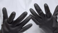 Hands in black butyl rubber gloves of a person wearing white lab coat.