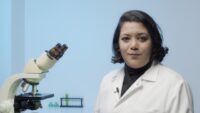 Girl smiling in white lab coat with microscope.