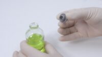 Small glass bottle with green liquid and the opened lid held in the hand.