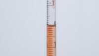 Red-orange coloured cell culture medium in 10 ml serological pipette that is held vertically.