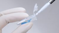 Micropipette used to pipette blue solution into microcentrifuge tube held by hand wearing sterile cell culture gloves.