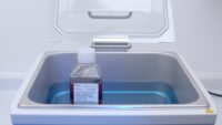 Waterbath with the lid open containing blue water and a bottle with red cell culture medium.