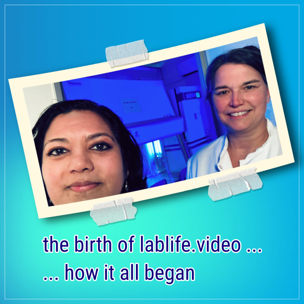 Asmita and Adelheid in white lab coats, a cell culture facility in blue light in the background with a sterile workbench and the UV light turned on.
