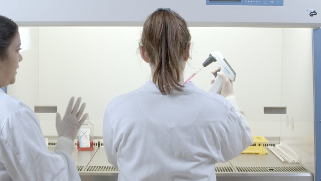 Two women in white lab coats, the trainee and the other giving instructions, a typical one-on-one training situation in the cell culture lab .