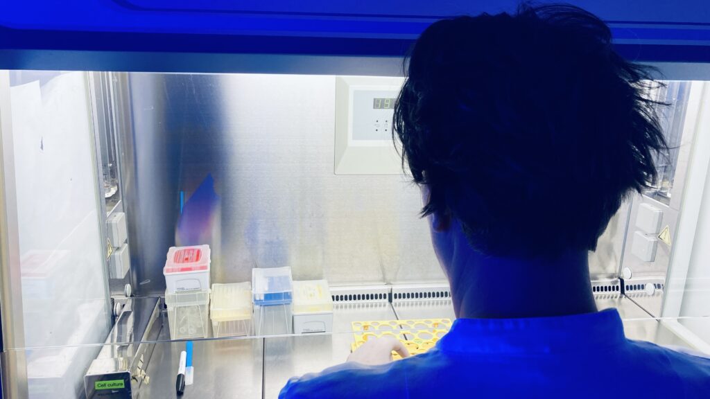 A mad looking scientist wearing a white lab coat, working in a sterile work bench in the cell culture lab in mysterious blue light.