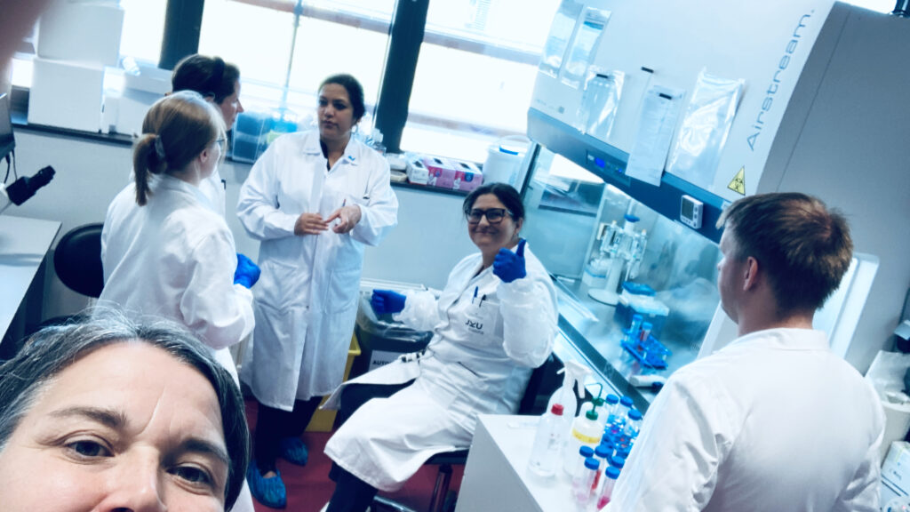 Researchers in white lab coats working in a cell culture laboratory, pipetting and discussing matters regarding cell culture work.