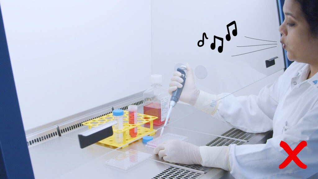 A person in white lab coat working in the sterile workbench, pipetting with a micropipette and whistling a tune at the same time – bad practices.