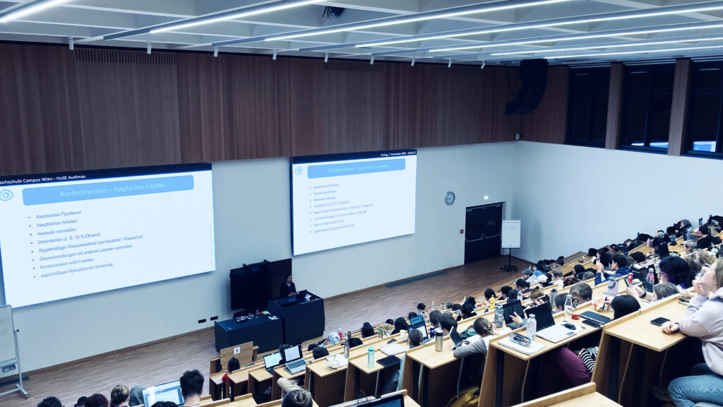 Students in Audi Max of University of Applied Sciences Vienna listening to lecture on cell culture practice given by Asmita Banerjee from lablife.video.
