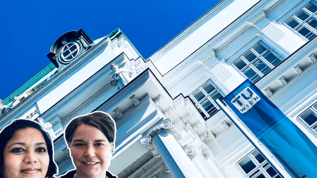 Adelheid Weidinger and Asmita Banerjee in front of white TU Wien building with dark blue sky.