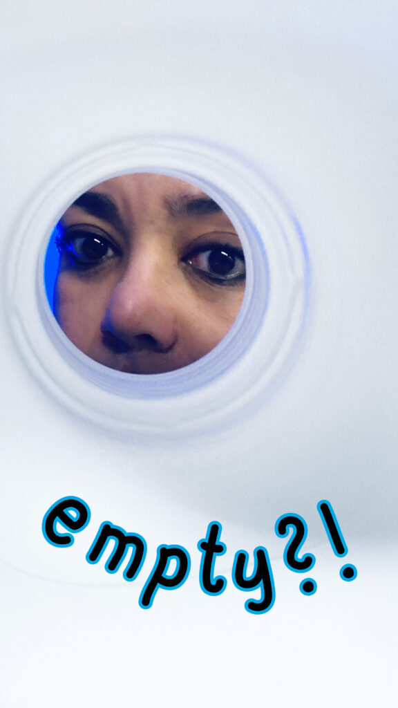 Women in white lab coat peeking into an empty chemical substance container, disappointed, picture taken from inside the container.